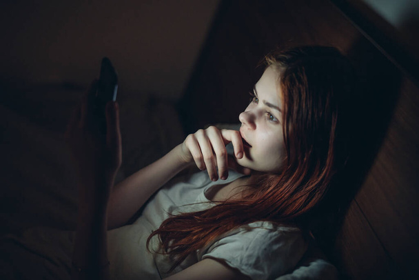 γυναίκα πριν από το κρεβάτι με ένα τηλέφωνο στα χέρια της εθισμό ανάγνωση ειδήσεων - Φωτογραφία, εικόνα