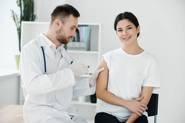 the doctor injects the covid-19 vaccine into the shoulder of the patient in a white t-shirt on a light background - Zdjęcie, obraz