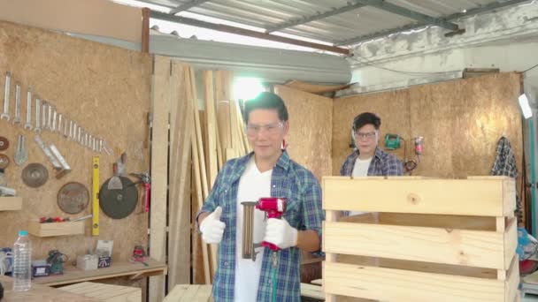 Deux menuisiers travaillent dans une usine de bois. Le menuisier fixe un tuyau d'air à un pistolet à clous pour conduire le bois automatiquement. - Séquence, vidéo