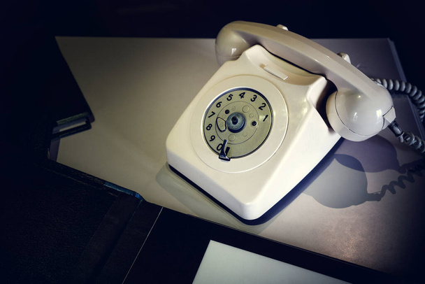 Закройте стационарный белый телефон на деревянном столе в темной комнате бумагой для связи с нами. Старомодный старинный винтажный телефон. - Фото, изображение