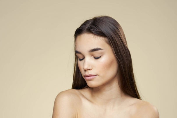 Mujer con los hombros desnudos pelo oscuro piel limpia maquillaje beige fondo - Foto, imagen