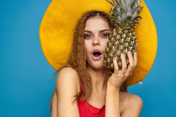 Γυναίκα σε κίτρινο καπέλο με ανανά στα χέρια συναισθήματα διασκέδαση τρόπο ζωής καλοκαίρι φρούτα μπλε φόντο - Φωτογραφία, εικόνα