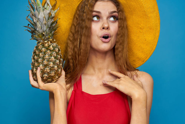 Жінка в жовтому капелюсі з ананасом в руках емоції веселий спосіб життя літні фрукти синій фон
 - Фото, зображення
