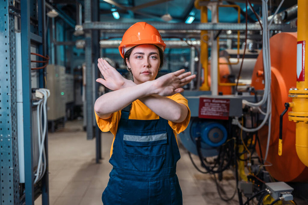 Retrato de una joven trabajadora con uniforme de trabajo y casco, brazos cruzados. En el fondo hay una sala de calderas. El concepto de producción industrial y equilty. - Foto, imagen