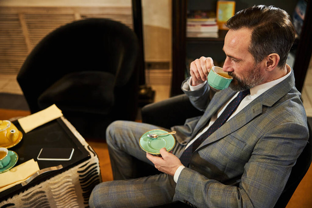 Сконцентрированный, хорошо одетый джентльмен наслаждается кофе-брейком - Фото, изображение