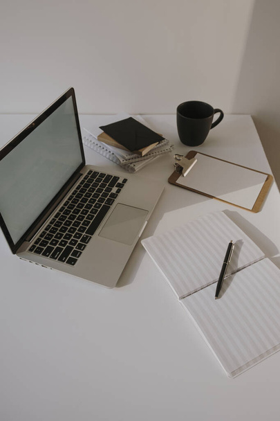 Laptop na mesa com xícara de café, folha de papel contra a parede branca. Espaço de trabalho minimalista do escritório em casa. - Foto, Imagem