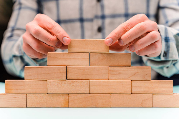 A man in a shirt builds a pyramid of wooden blocks, a concept of development and strategy in business - Photo, Image