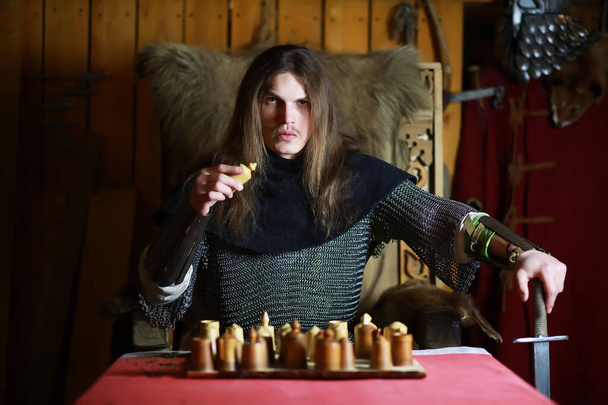 Een machtige held met lang haar in een maliënkolder in een oude hal. Middeleeuwse krijger in de ridderkamers. - Foto, afbeelding