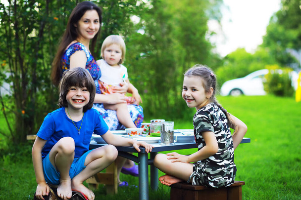 Uma jovem família grande em um piquenique em uma manhã de verão. Uma bela mãe com filhos está tomando café da manhã no parque. - Foto, Imagem