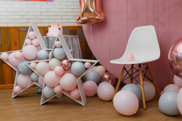 Prachtige feestelijke decoraties, roze en grijze ballonnen, houten sterren, witte stoel en nummer één ballon op houten ronde achtergrond. Klein 1 jaar oud meisje verjaardag feest foto zone. - Foto, afbeelding