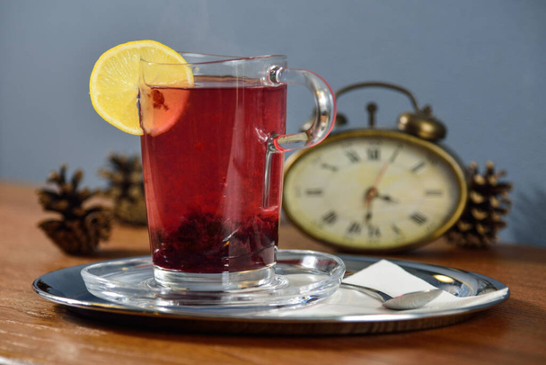 Tasse en verre de thé au citron sur une table en bois avec un réveil en arrière-plan - Photo, image