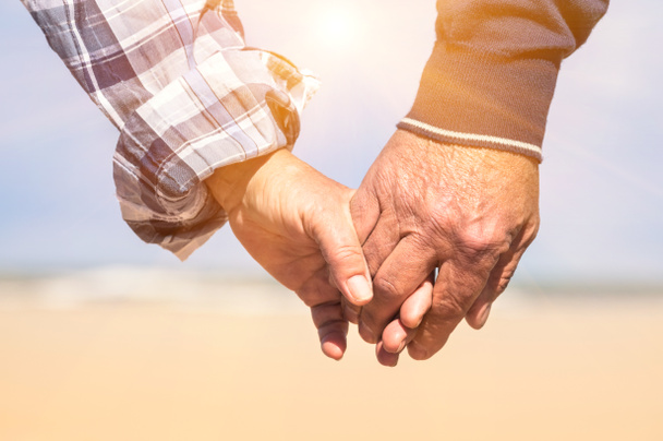 Verliebte Senioren spazieren an einem romantischen, sonnigen Tag Händchen haltend am Strand - Konzept der Liebe und der Familienzusammenführung - Foto, Bild