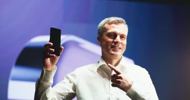 Hombre maduro apuntando al nuevo smartphone durante la presentación - Metraje, vídeo