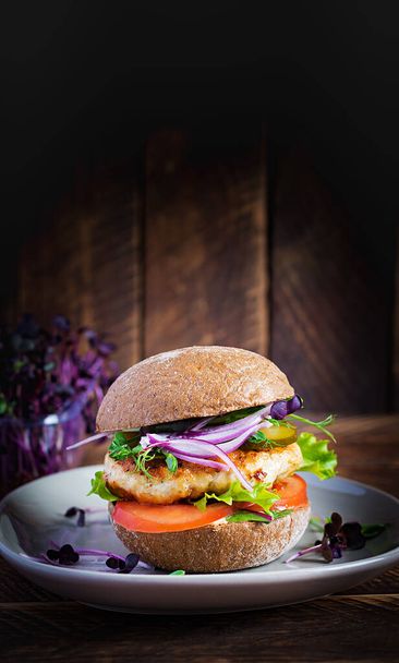 Hamburger. Sandwich with chicken burger, tomatoes,  pickled cucumber and red onion. Fresh tasty chicken burger on wooden table. - Photo, Image