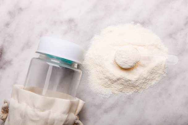 Montón de polvo de proteína blanca con cuchara dosificadora y botella sobre fondo de mármol. - Foto, Imagen