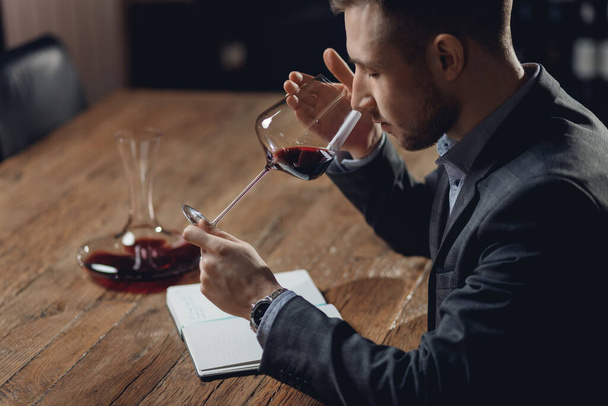 Sommelier compiles tasting card of alcohol for restaurant, evaluates red wine in glass - Photo, Image