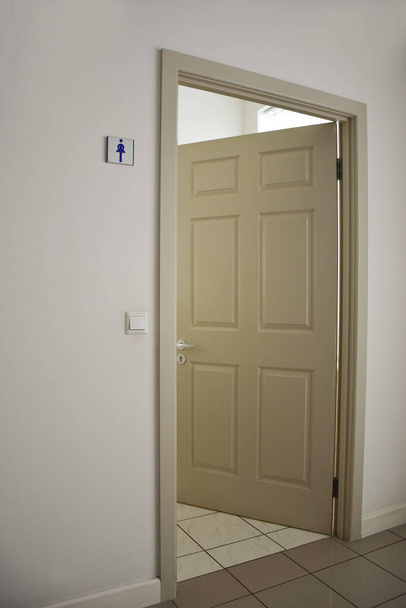 Une porte ouverte sur les toilettes pour femmes avec un panneau sur le mur. Le sol est recouvert de tuiles. Cadre en perspective - Photo, image