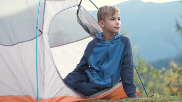 Menino feliz descansando em uma tenda turística no acampamento da montanha apreciando vista da bela natureza de verão. Caminhadas e conceito ativo de estilo de vida. - Filmagem, Vídeo