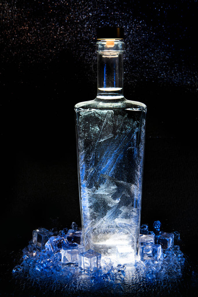 Un recipiente, una botella cerrada con una tapa con un patrón de heladas, cristales de hielo, fragmentos de hielo sobre un fondo oscuro - Foto, Imagen