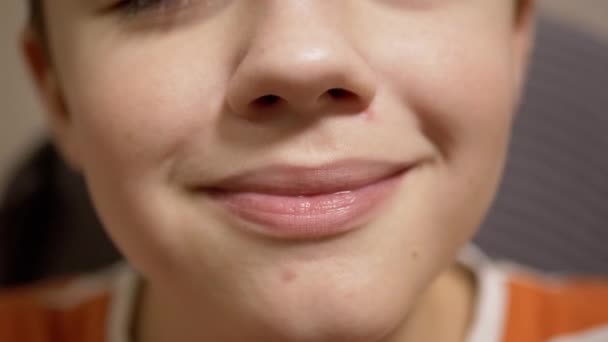 Positiivinen teini-ikäinen poika, jolla on kauniit pulleat huulet, hymyile. Lähemmäs. Osa kasvoja - Materiaali, video