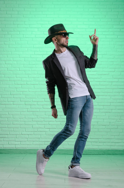 fashionable stylish man in a jacket and a cowboy hat poses in the studio - Foto, afbeelding