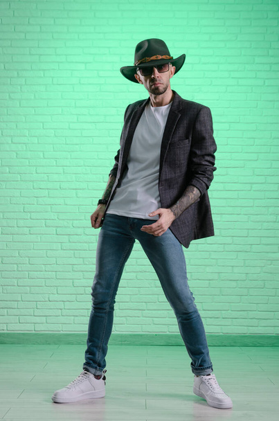 divatos, elegáns férfi zakóban és cowboy kalapban pózol a stúdióban. - Fotó, kép