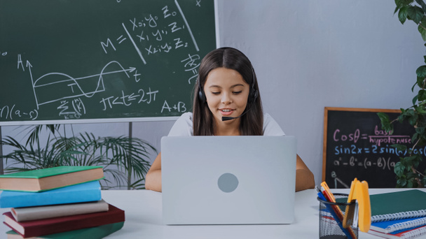щасливий школяр в гарнітурі дивиться на ноутбук під час онлайн навчання вдома
 - Фото, зображення
