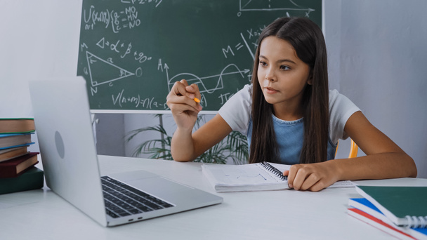 дівчина тримає ручку і дивиться на ноутбук під час онлайн-навчання вдома
 - Фото, зображення