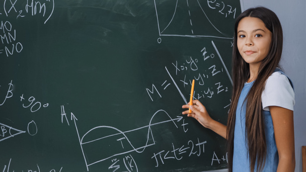 Kind hält Stift in der Hand und zeigt mathematische Formeln auf Kreidetafel  - Foto, Bild