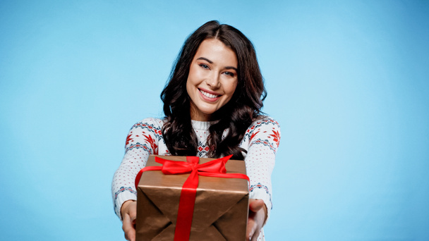Smiling woman in sweater holding present on blue background - Fotografie, Obrázek