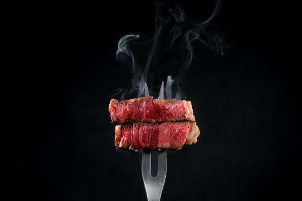 Sliced and steaming rare rib eye steak on a fork on a dark background - Photo, Image