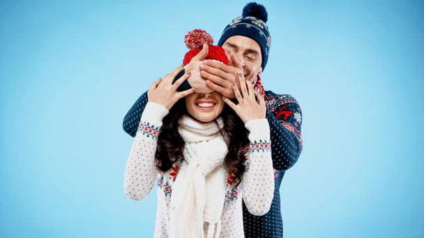 Man in hat covering eyes to smiling girlfriend on blue background - Foto, Imagen