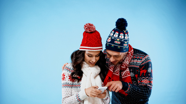 Smiling couple in warm clothes using smartphone on blue background - Photo, Image