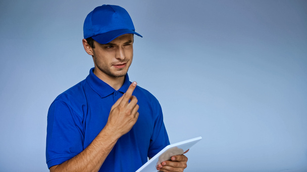 homme de livraison réfléchi avec tablette numérique pointant du doigt tout en regardant loin isolé sur bleu - Photo, image