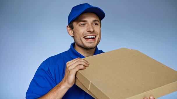 excited delivery man looking away while holding pizza boxes isolated on blue - Fotó, kép