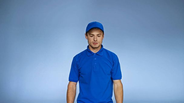 trastornado repartidor en uniforme de pie aislado en azul - Foto, Imagen