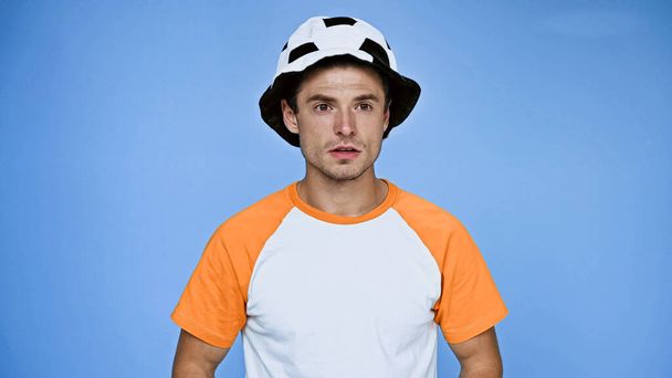 молодий чоловік у футбольному капелюсі дивиться в сторону ізольовано на синьому
 - Фото, зображення