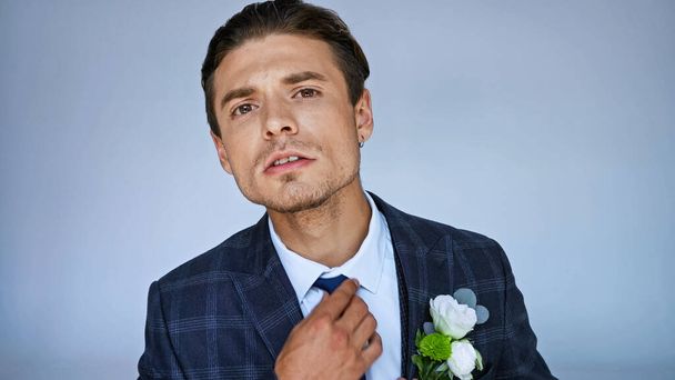 worried fiance adjusting tie while looking at camera isolated on blue - Foto, Imagem