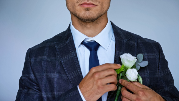 partial view of elegant bridegroom fixing boutonniere isolated on blue - Photo, Image