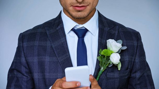 partial view of smiling bridegroom messaging on mobile phone isolated on blue - Foto, immagini