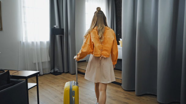 Rückansicht einer Frau in Kleid und Jacke, die im Hotelzimmer spaziert - Foto, Bild