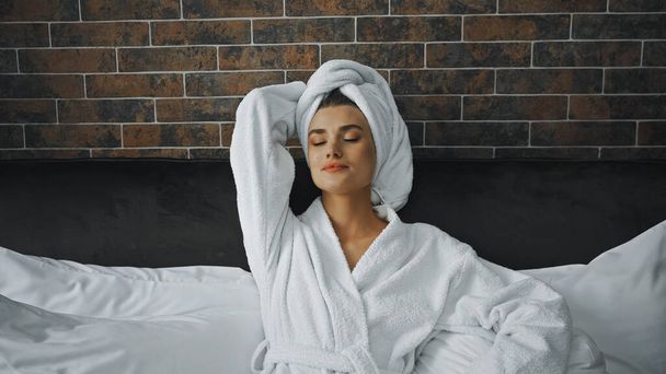 woman with closed eyes in white towel resting on bed in hotel room - Valokuva, kuva