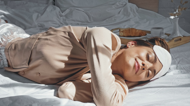mujer complacida con los ojos cerrados acostado en la cama cerca de bandeja con desayuno - Foto, imagen