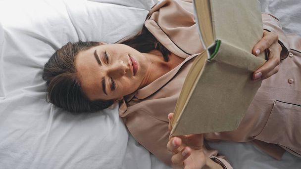 Frau liest Roman, während sie im Bett liegt - Foto, Bild