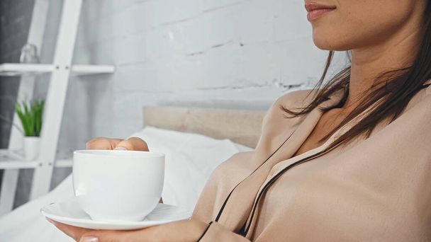 cropped view of woman holding saucer and cup of coffee - Foto, Bild
