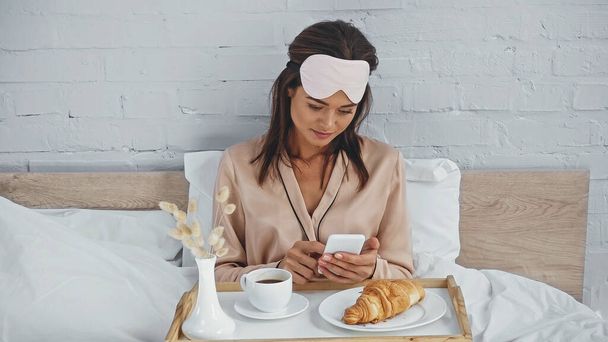 Esmer bir kadın akıllı telefondan lezzetli bir kahvaltıyla birlikte tepsinin yanında mesajlaşıyor.  - Fotoğraf, Görsel