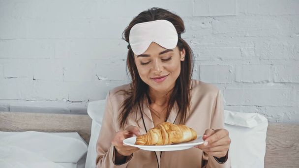 mujer feliz con la máscara de ojo placa de retención con croissant sabroso  - Foto, imagen