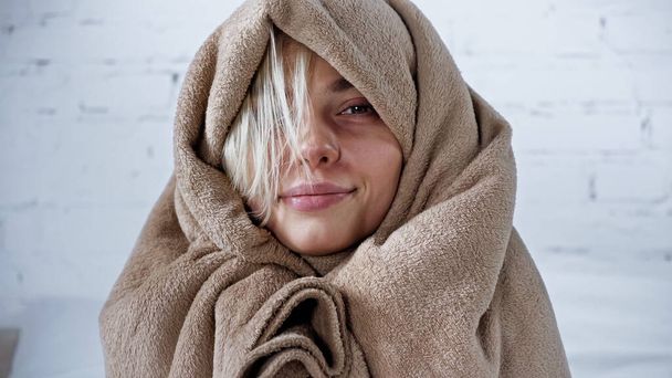 diseased woman, wrapped in warm blanket, smiling at camera in bedroom - 写真・画像