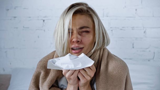 sick woman holding paper napkin while sneezing in bedroom - Photo, Image
