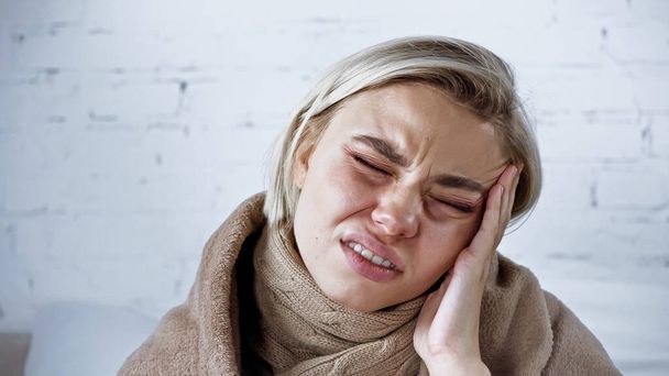 mujer enferma frunciendo el ceño con los ojos cerrados mientras sufre de dolor de cabeza en el dormitorio - Foto, Imagen